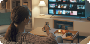 Woman in sweater selects a show on TV in cozy, warmly lit living room.