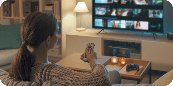 Woman in sweater selects a show on TV in cozy, warmly lit living room.